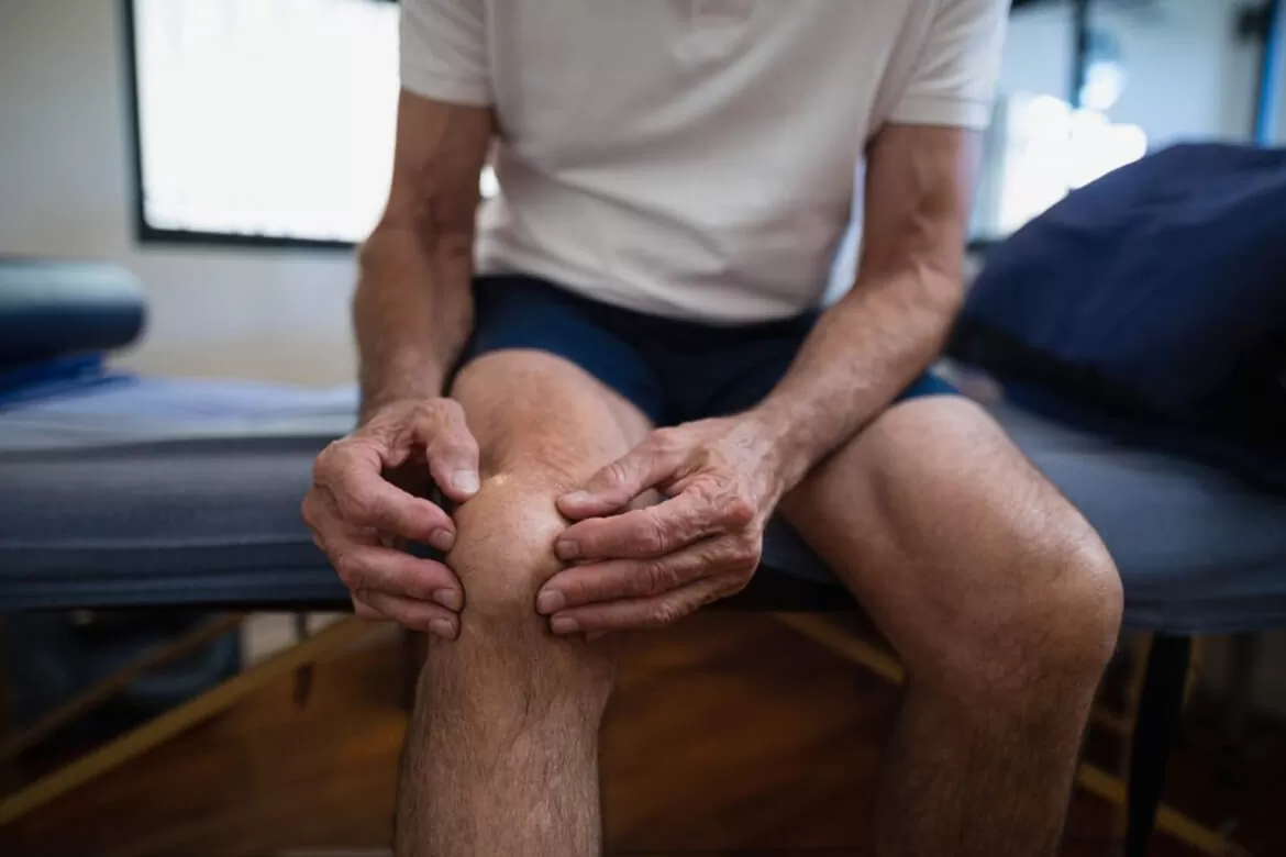 o persoană care se ține cu mâna de articulații și ligamentele din zona genunchiului pentru că nu și-a luat suplimentele necesare